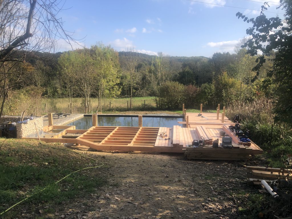 Réalisation en cour de chantier d'une terrasse en bois autour d'un piscine naturelle bassin de baignade